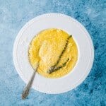 a bowl of polenta topped with parmigiano reggiano cheese and a sprig of thyme.