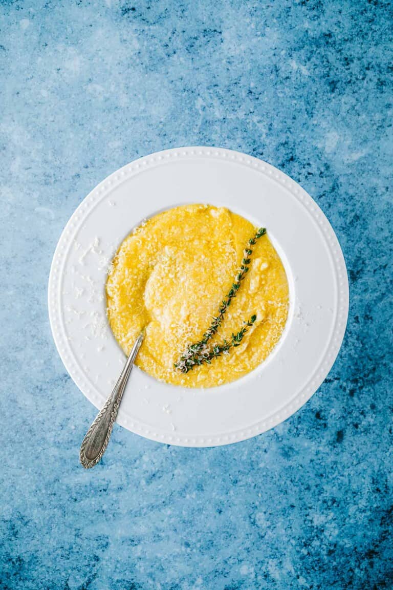 a bowl of polenta topped with parmigiano reggiano cheese and a sprig of thyme.