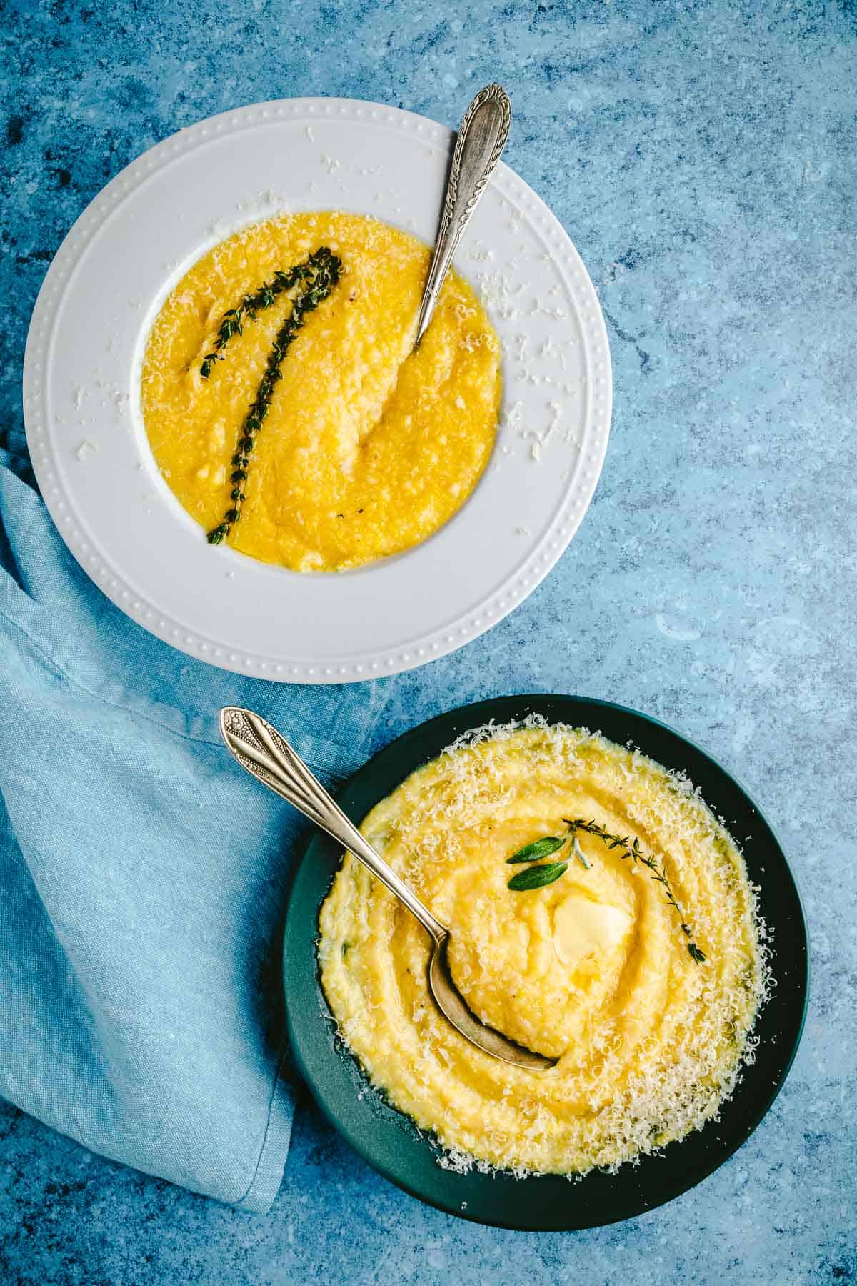 two bowls of polenta topped with parmigiano reggiano cheese and a sprig of thyme next to a cloth napkin.
