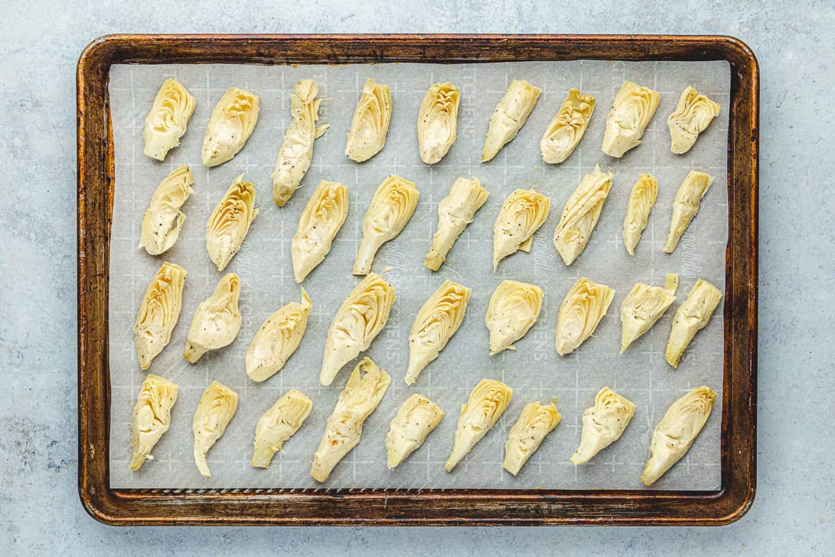 Canned artichoke hearts that have been spread on a sheet tray and seasoned with salt and pepper.