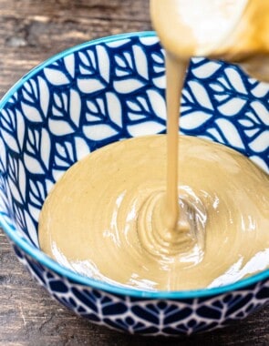 Tahini being poured from the jar into a blue bowl.