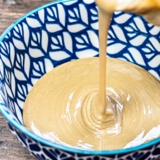 Tahini being poured from the jar into a blue bowl.