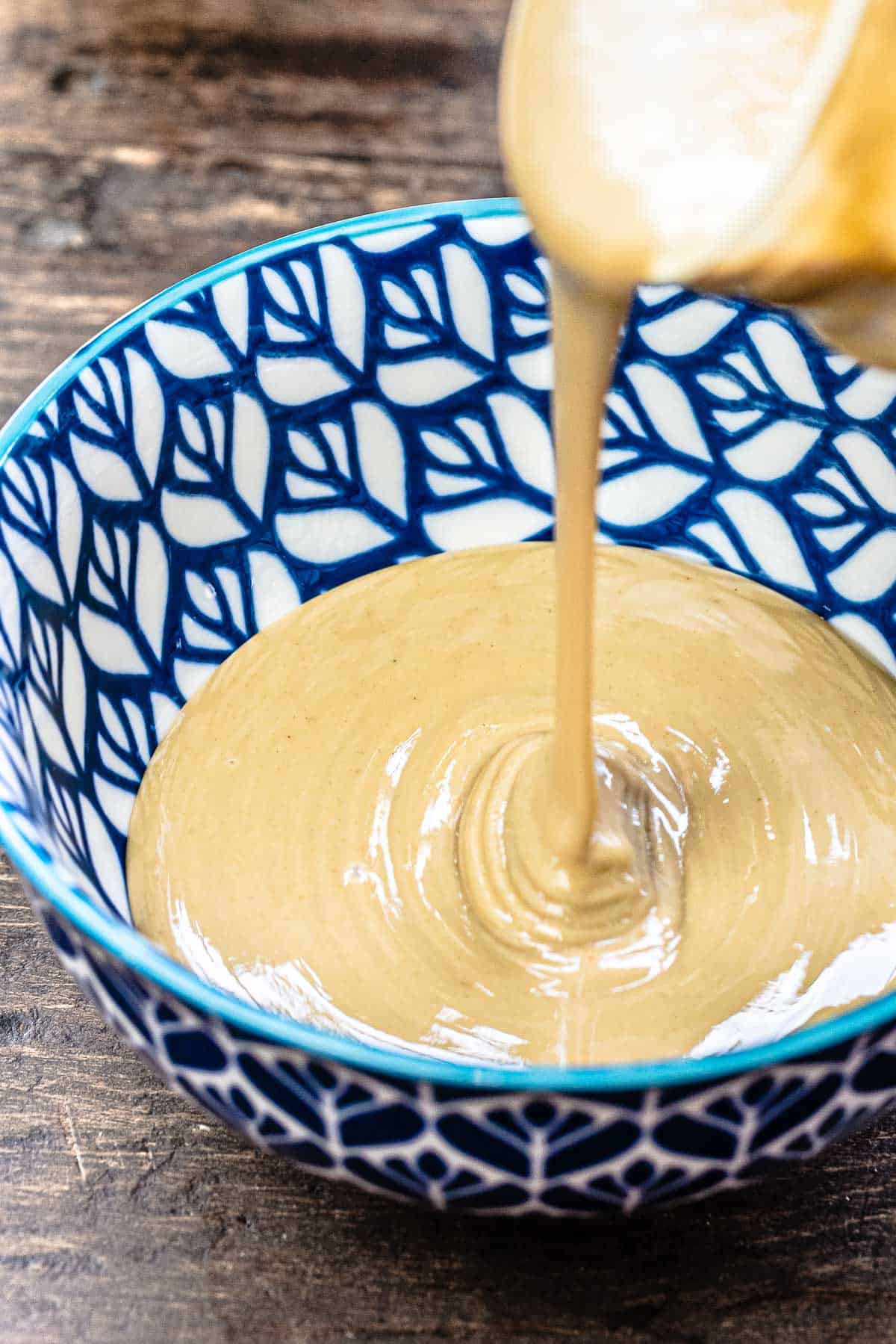 Tahini being poured from the jar into a blue bowl.