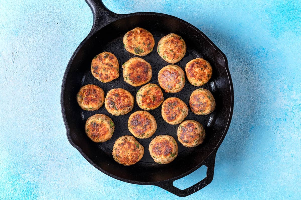 chicken piccata meatballs browning in a cast iron skillet.