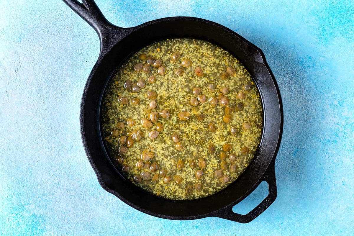 piccata sauce simmering in a cast iron skillet.