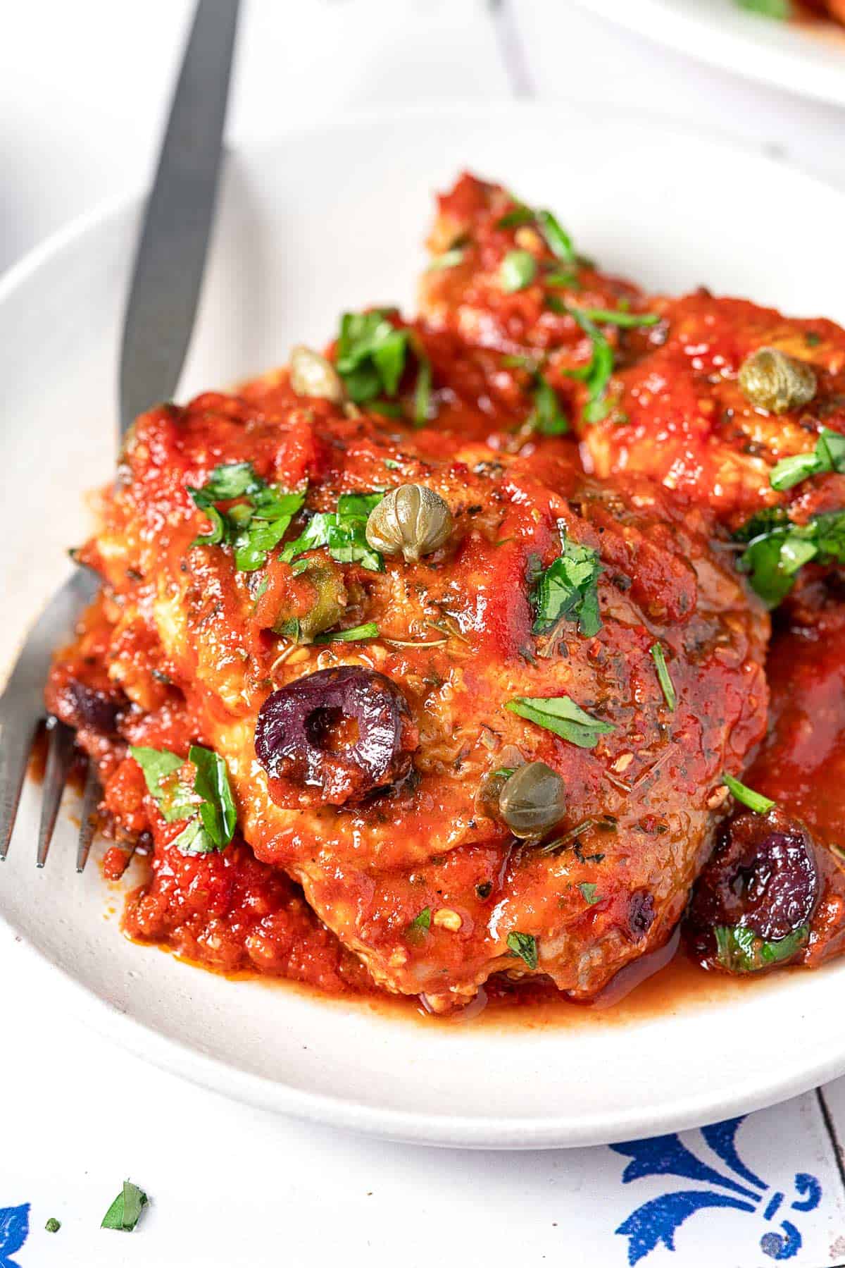 two pieces of chicken puttanesca on a plate with a fork.