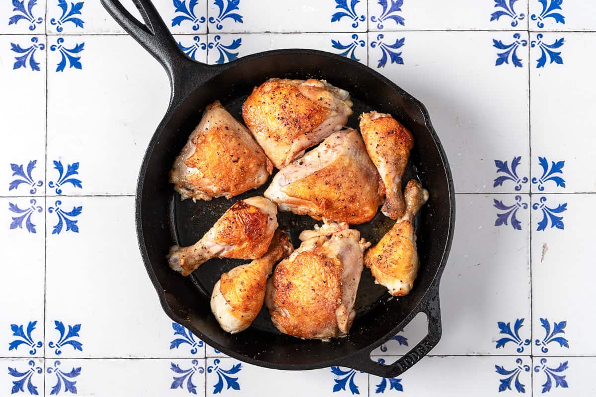 8 pieces of bone-in skin-on chicken browning in a cast iron skillet.
