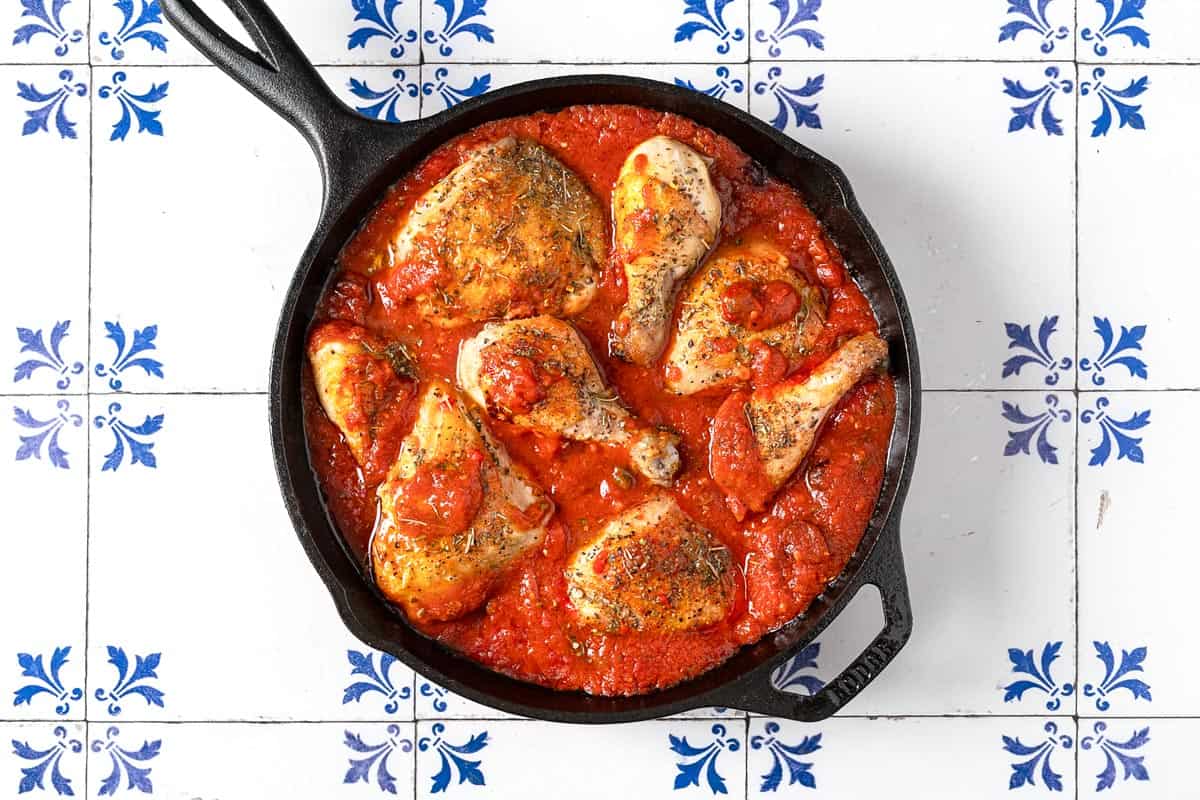 pieces of browned chicken simmering in a tomato-based sauce.