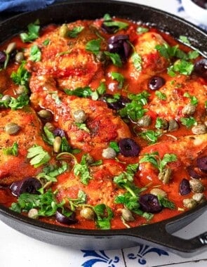 chicken puttanesca topped with parsley, capers and kalamata olives in a cast iron skillet.