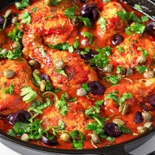 chicken puttanesca topped with parsley, capers and kalamata olives in a cast iron skillet.