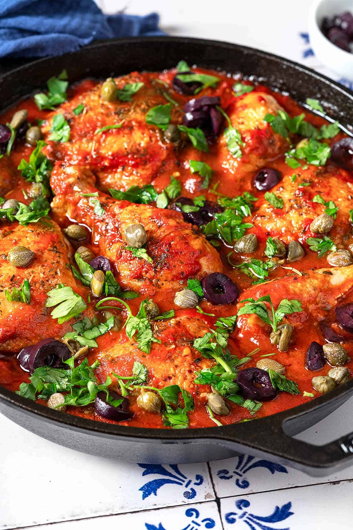 chicken puttanesca topped with parsley, capers and kalamata olives in a cast iron skillet.