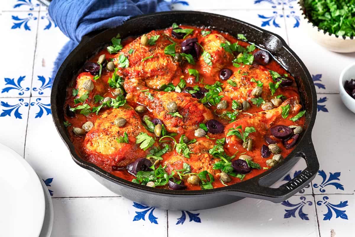 chicken puttanesca topped with parsley, capers and kalamata olives in a cast iron skillet.