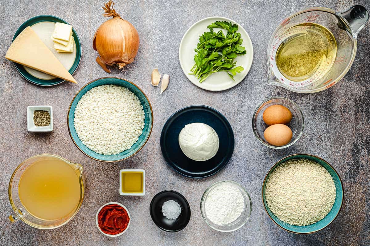ingredients for arancini Italian fried risotto including parmesan cheese, butter, onion, garlic, parsley, olive oil, pepper, arborio rice, mozzarella, salt, chicken stock, tomato paste, flour, eggs, and breadcrumbs.
