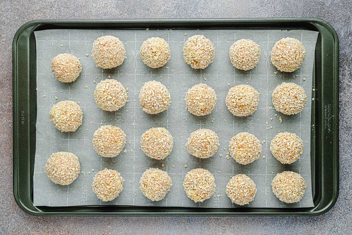 breaded arancini italian fried risotto balls on a parchment lined baking sheet.