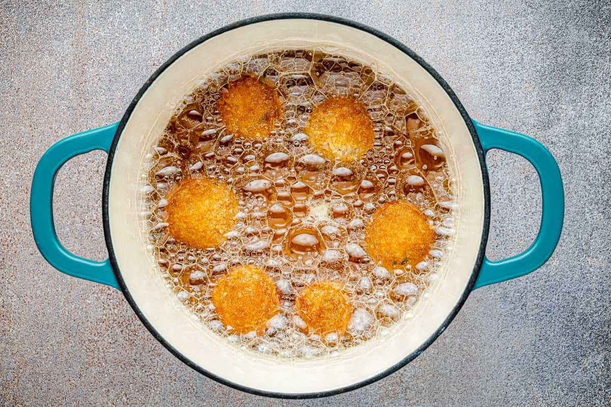 arancini italian fried risotto balls frying in a pot of oil