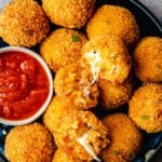 two arancini italian fried risotto balls opened up on a pile of other arancini balls on a plate with a bowl of marinara.