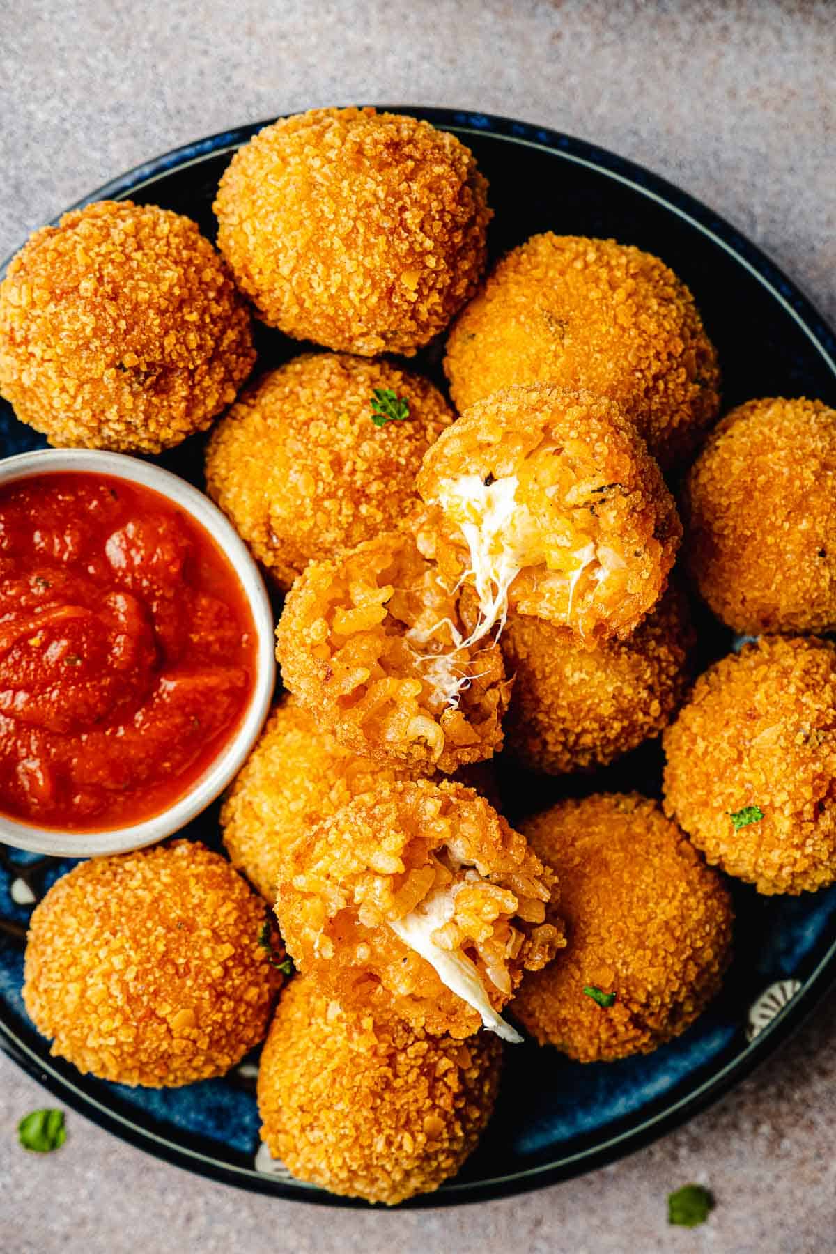 two arancini italian fried risotto balls opened up on a pile of other arancini balls on a plate with a bowl of marinara.