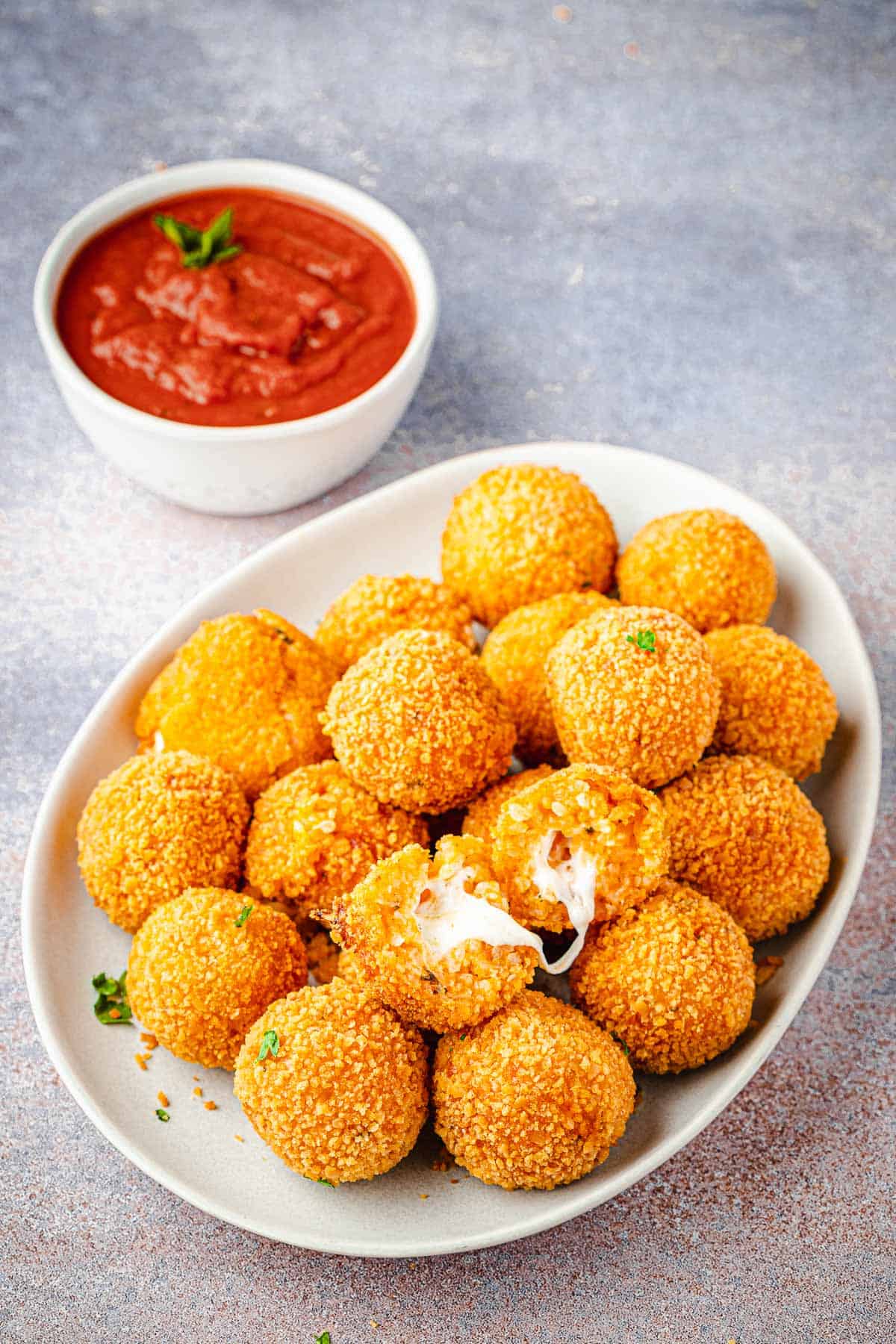 arancini italian fried risotto balls on a plate next to a bowl of marinara.