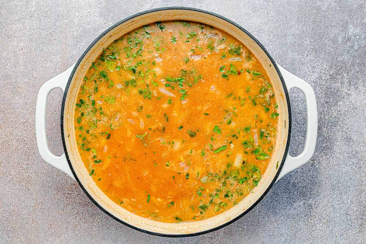 arborio rice starting to cook in a pot in broth with salt, pepper, parsley tomato paste and butter.