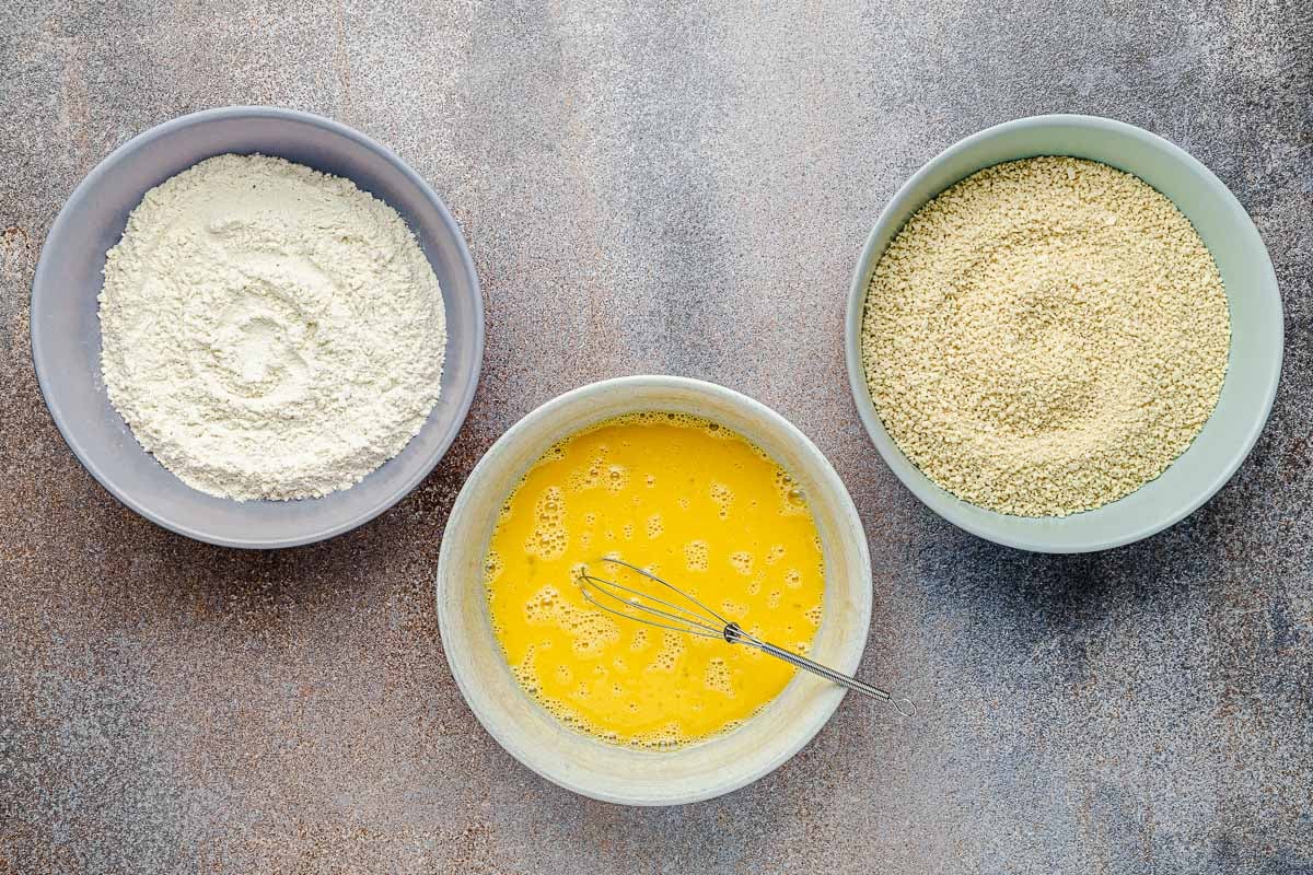 ingredients for a breading station including a bowl of whisked eggs, a bowl of flour and a bowl of panko breadcrumbs.