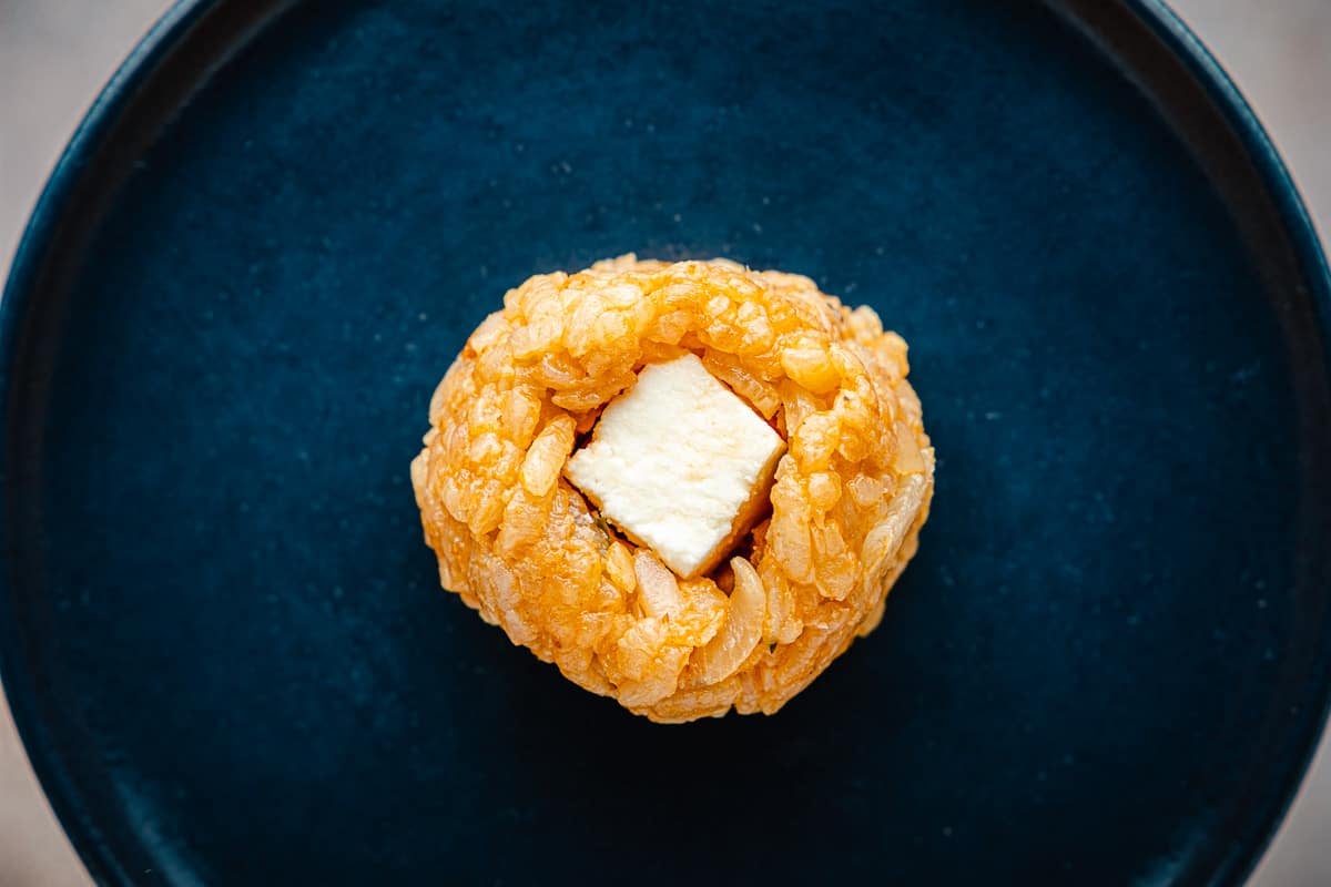 a cube of mozzarella cheese stuffed into an unbreaded arancini italian risotto ball on a plate.