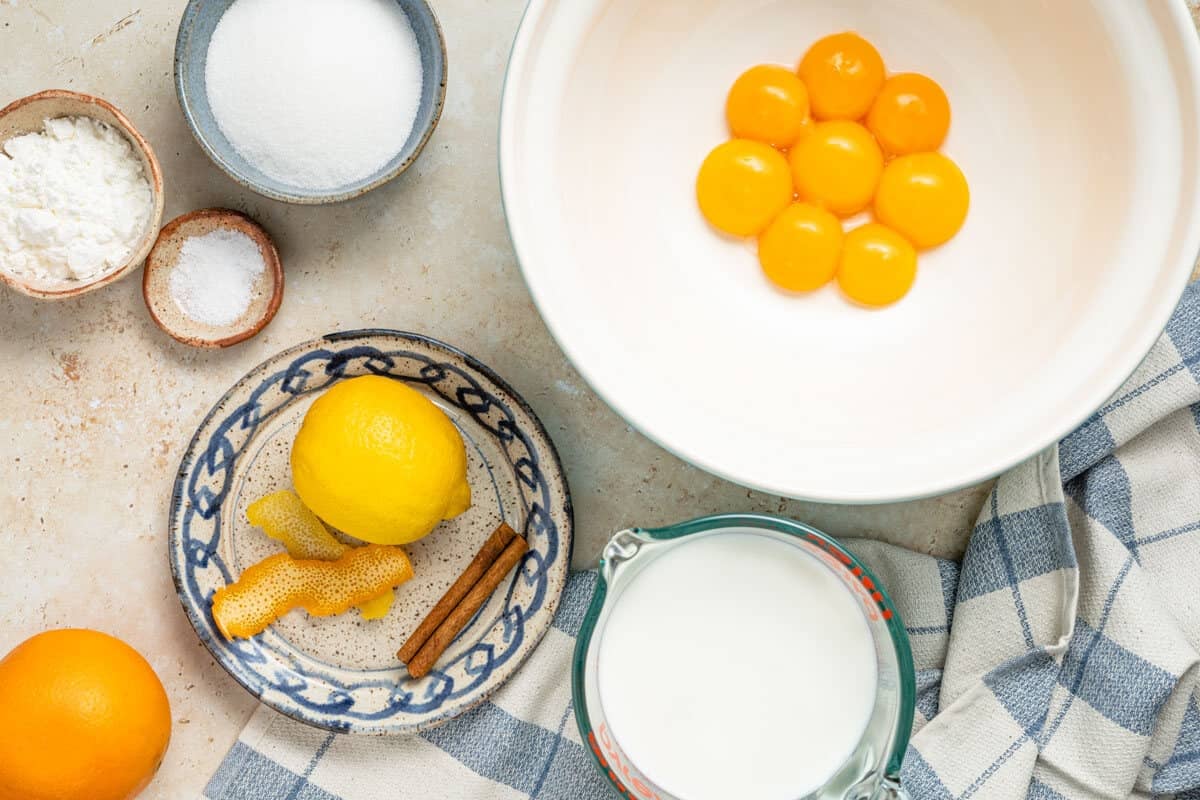 Ingredients for Crema Catalana, including egg yolks, sugar, cornstarch, salt, whole milk, citrus zest, and a cinnamon stick.