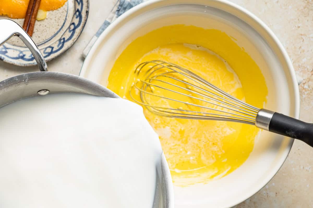 Warm milk being slowly whisked into eggs to temper them.