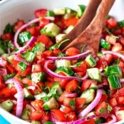 cucumber tomato salad in a bowl with wooden serving utensils.