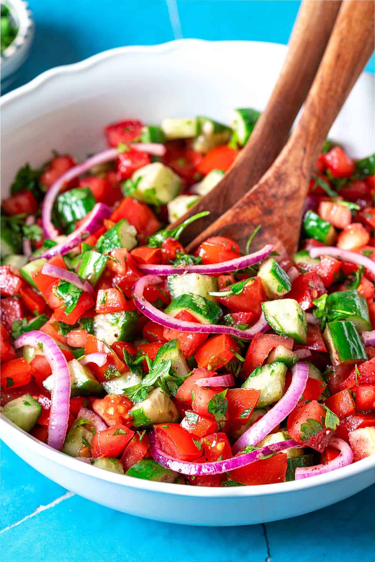 cucumber tomato salad in a bowl with wooden serving utensils.