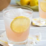 a glass of rose lemonade on a coaster, garnished with a lemon wheel.