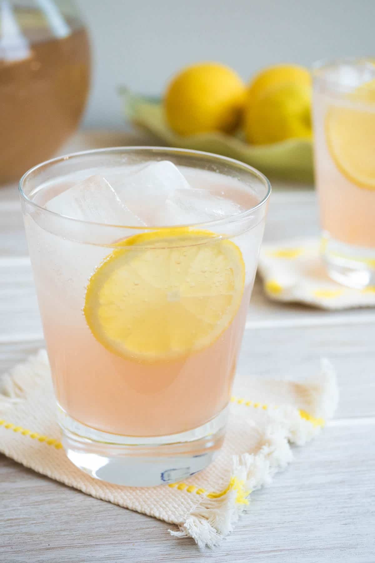 a glass of rose lemonade on a coaster, garnished with a lemon wheel.
