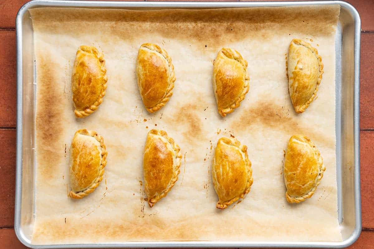 8 baked spanish beef empanadillas on a parchment paper lined baking sheet.