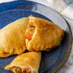 two baked empanadillas stacked on a plate, one is torn in half.