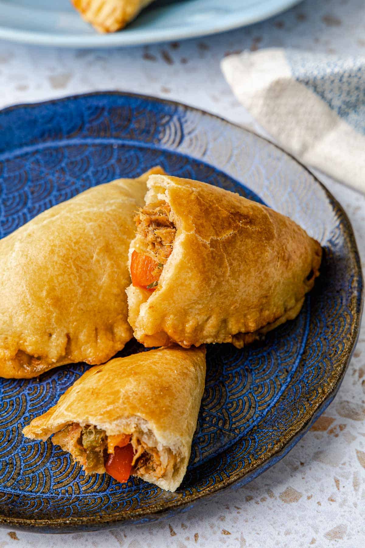 two baked empanadillas stacked on a plate, one is torn in half.