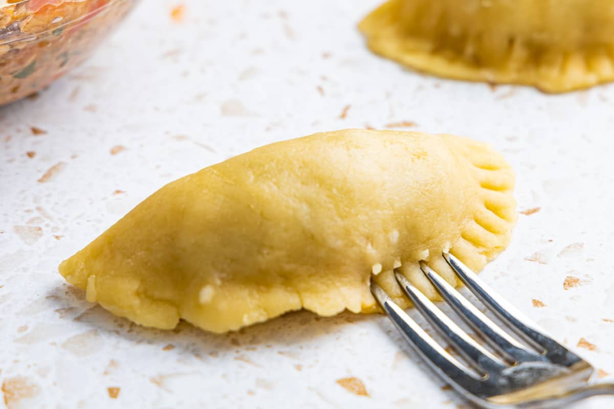 the edges of an unbaked tuna empanadilla being crimped with a fork.