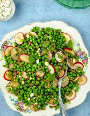 spring pea salad with sliced radishes and mint on a plate with a silver serving spoon next to a bowl of cubed feta cheese.