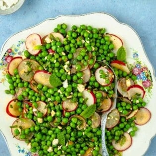 spring pea salad with sliced radishes and mint on a plate with a silver serving spoon next to a bowl of cubed feta cheese.