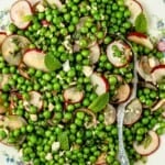 spring pea salad with sliced radishes and mint on a plate with a silver serving spoon.