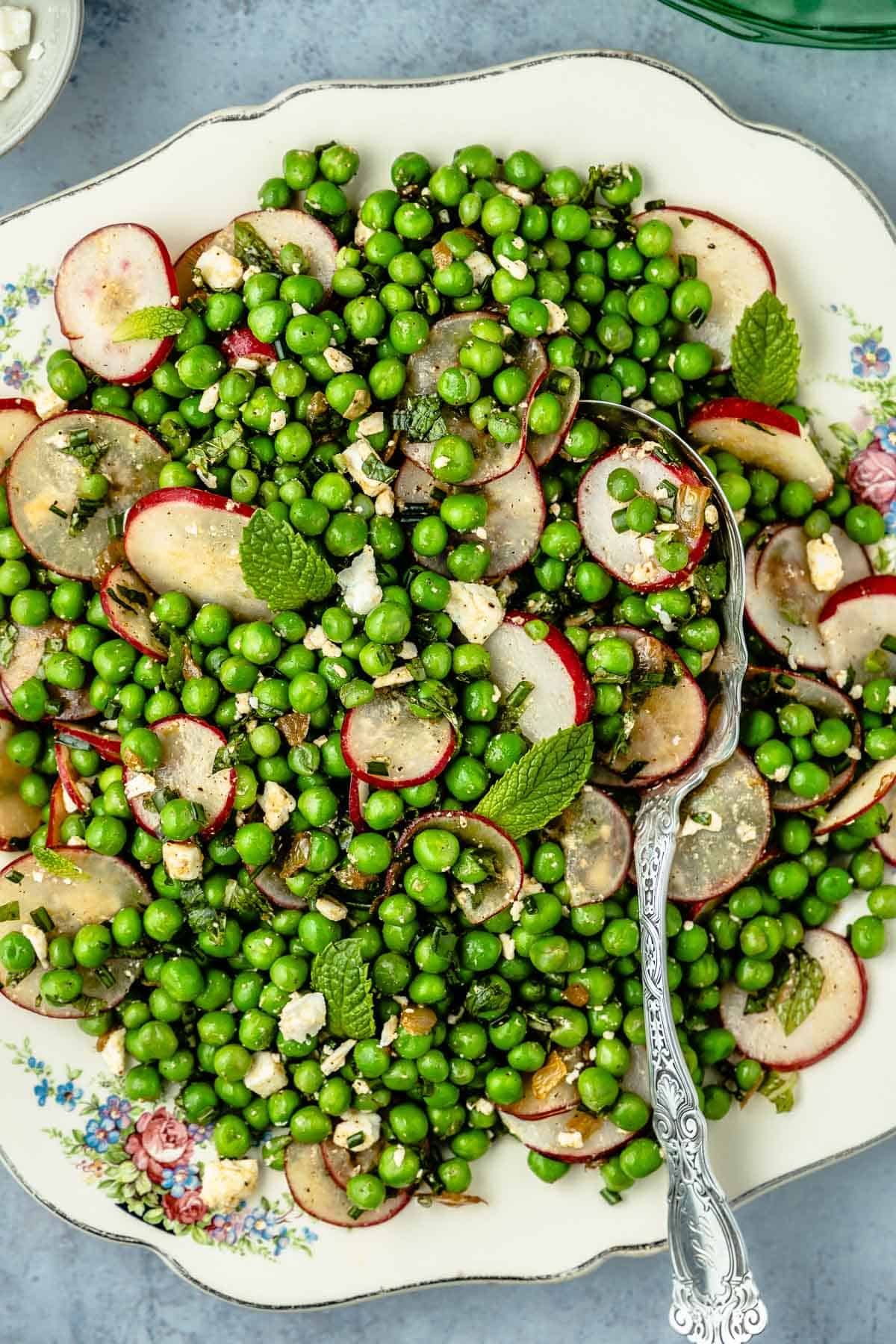 spring pea salad with sliced radishes and mint on a plate with a silver serving spoon.