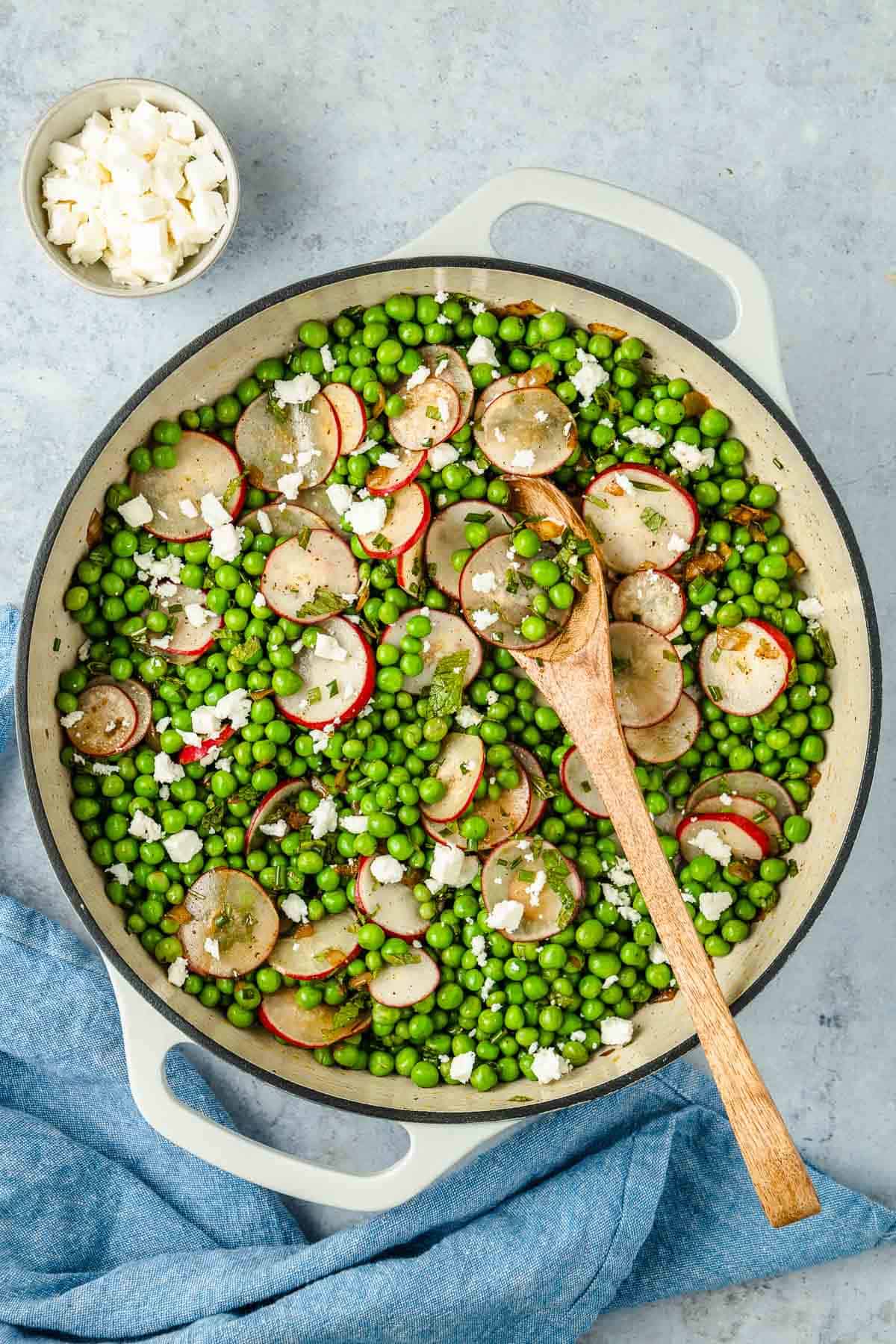 spring pea salad with sliced radishes and mint in a pot with a wooden spoon next to a bowl of cubed feta.