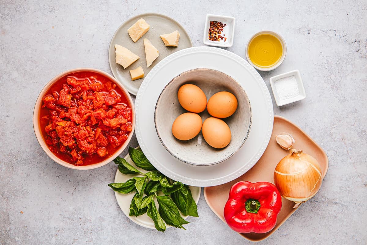 ingredients for eggs in purgatory including 4 eggs, olive oil, onion, garlic, red pepper flakes, red bell pepper, salt, canned diced tomatoes, basil, and grated parmigiano-reggiano cheese.