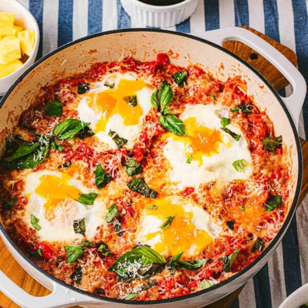 A skillet of eggs in purgatory next to a jar of jam and other various table settings.