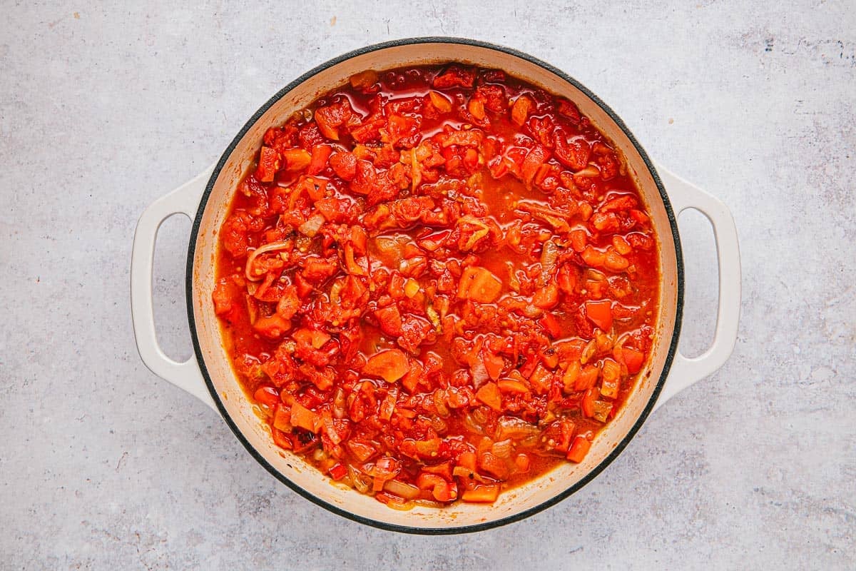 tomates, oignons, poivrons rouges et flocons de piment rouge mijotés dans une poêle.
