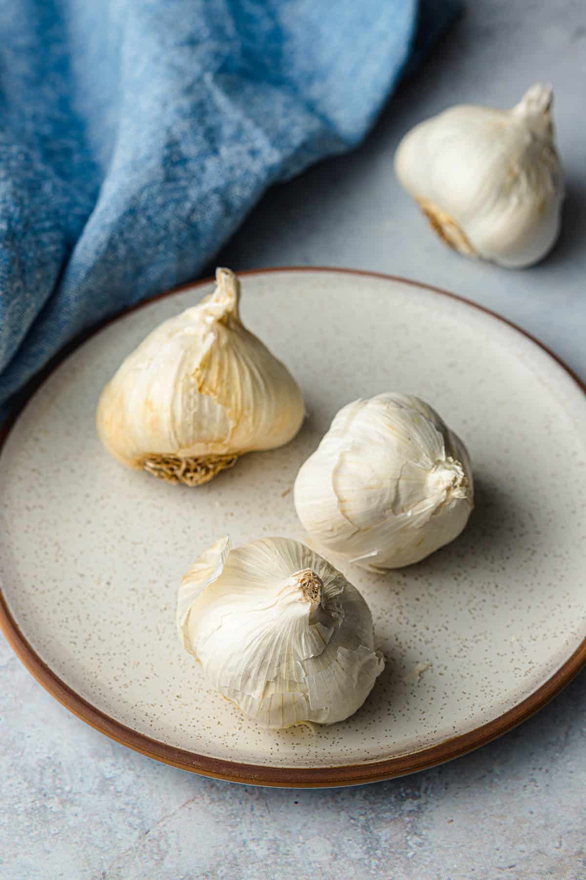 Three heads of garlic on a plate with a blue linen napkin in the background.