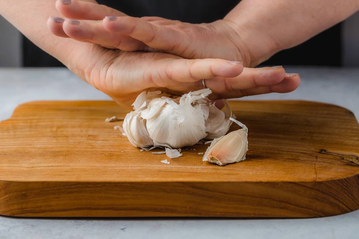 Person using two hands to press down on a head of garlic, separating the cloves.