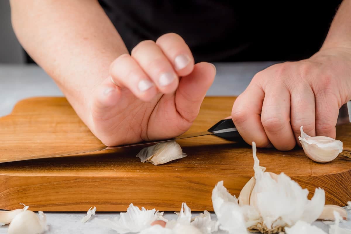 Person smashing garlic using the side of the knife and the palm of their hand.