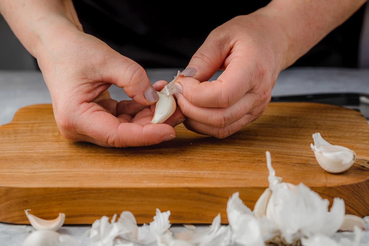 Person peeling garlic and exposing the clove.