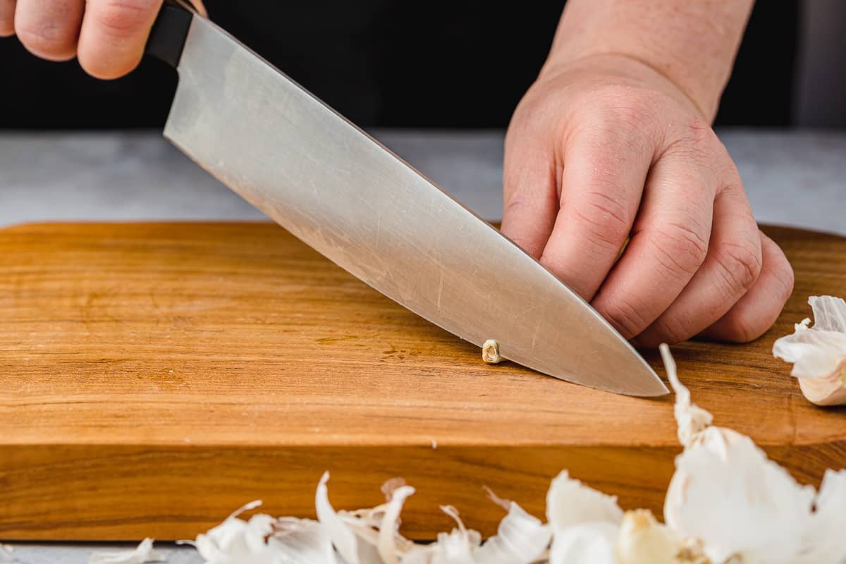 Person trimming off the end of garlic using a large chef's knife.