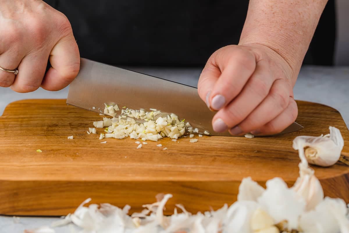 Close up of someone mincing garlic, with their left hand being used to steady the knife.
