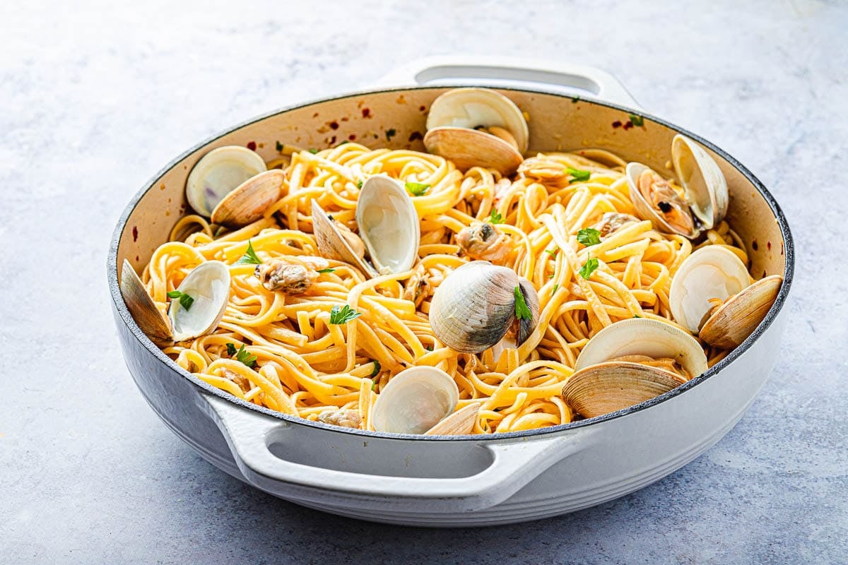 Linguini with clams in a shallow white pot with a garnish of fresh parsley.